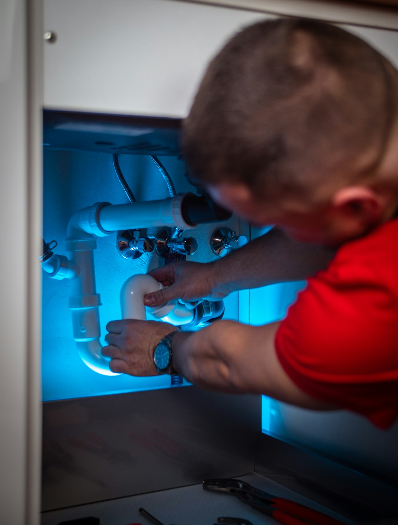 Мастер подключает сифон и подводку воды в тумбе под мойкой